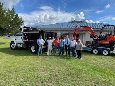 Image of dump truck and Trackhoe with Town employees and officials.